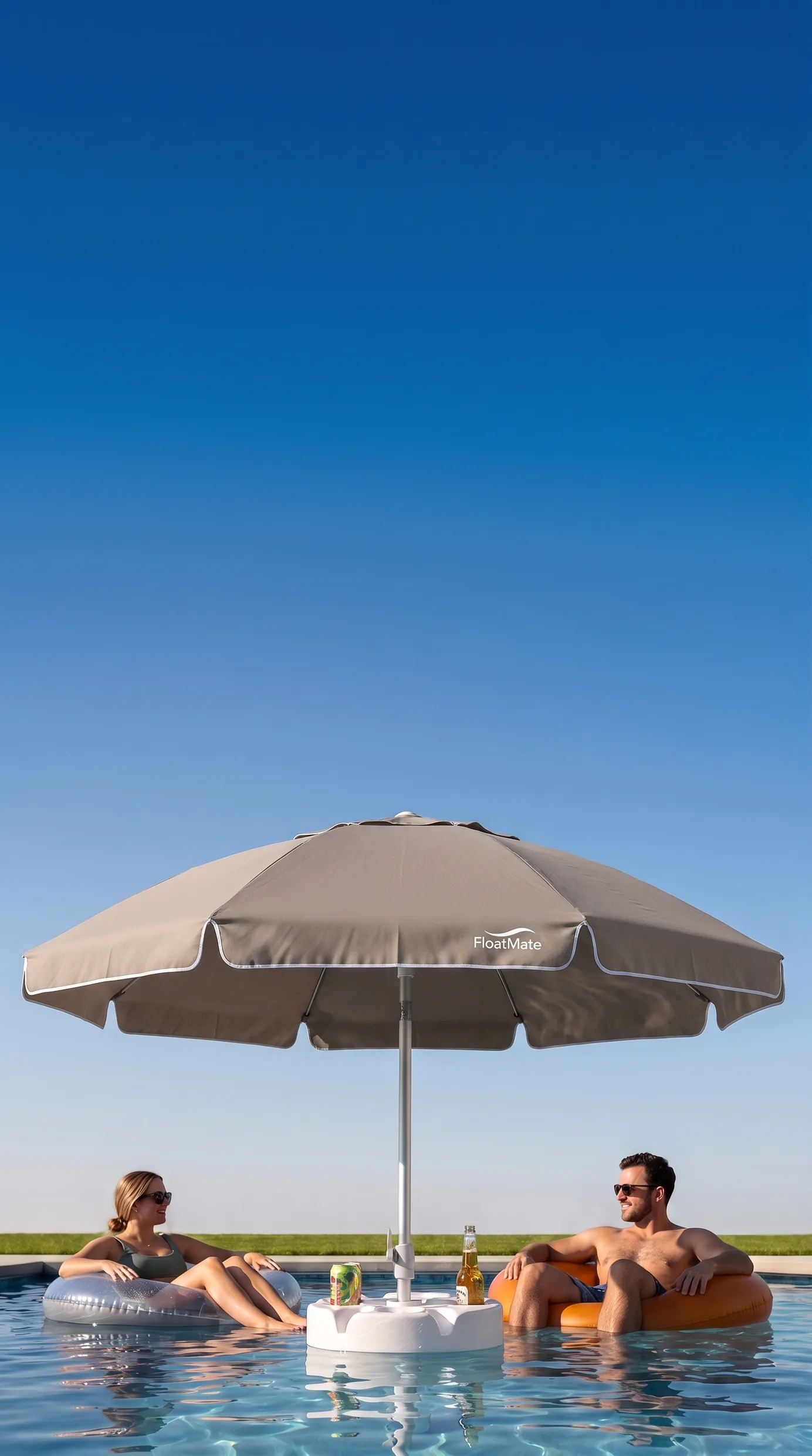 A woman and a man floating on pool rings either side of a FloatMate umbrella, cold drinks standing in its table, under a clear blue sky