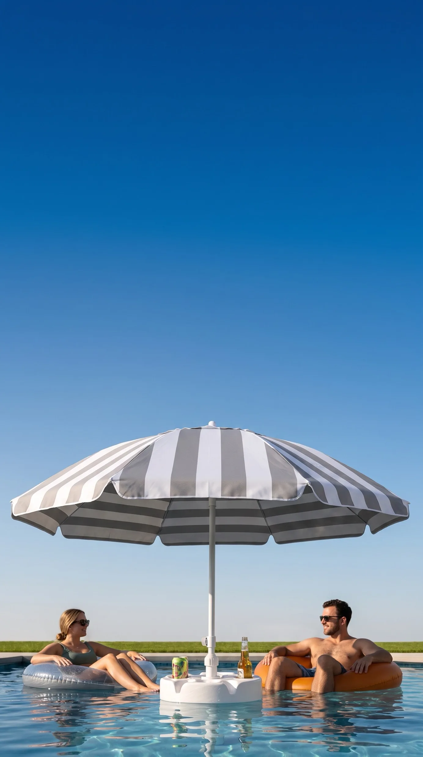 A woman and a man floating on pool rings either side of a FloatMate umbrella, cold drinks standing in its table, under a clear blue sky
